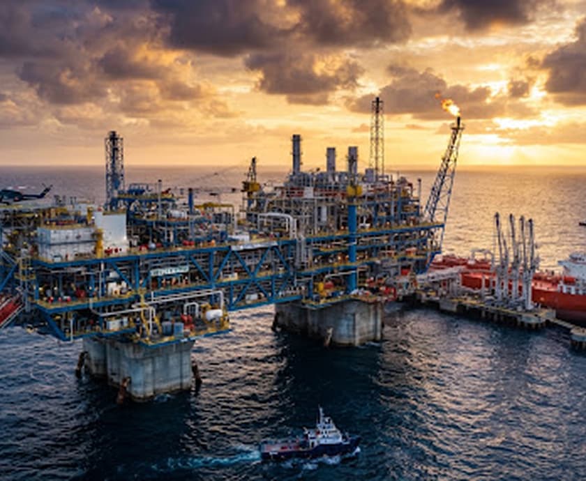 Plataforma petrolera marina al atardecer, con un buque tanque atracado y una lancha de apoyo